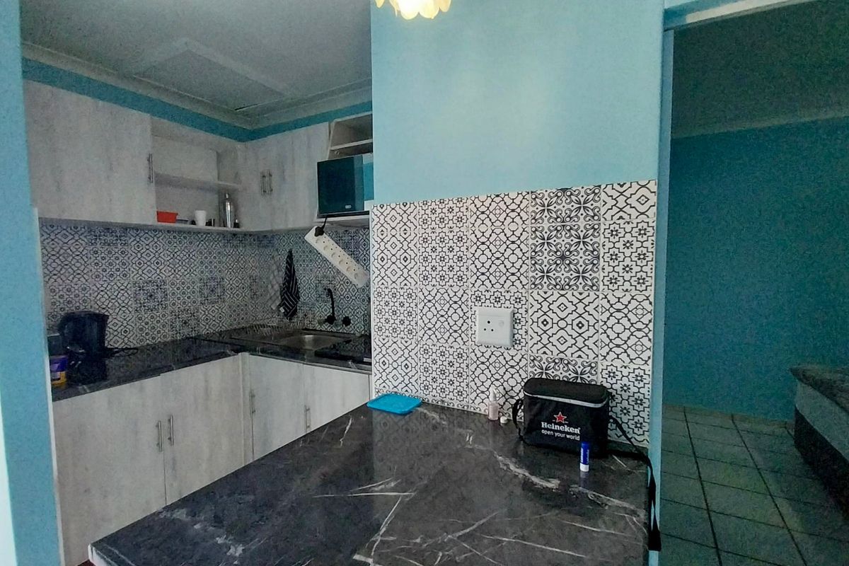 Compact kitchen featuring modern patterned tile backsplash, stone-look countertops, and light-toned cabinetry with integrated storage solutions.