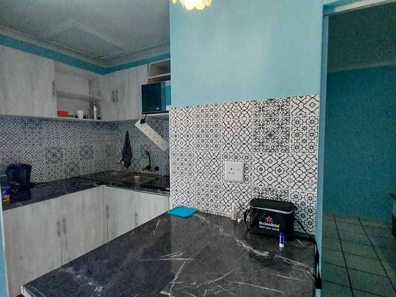 Compact kitchen featuring modern patterned tile backsplash, stone-look countertops, and light-toned cabinetry with integrated storage solutions.