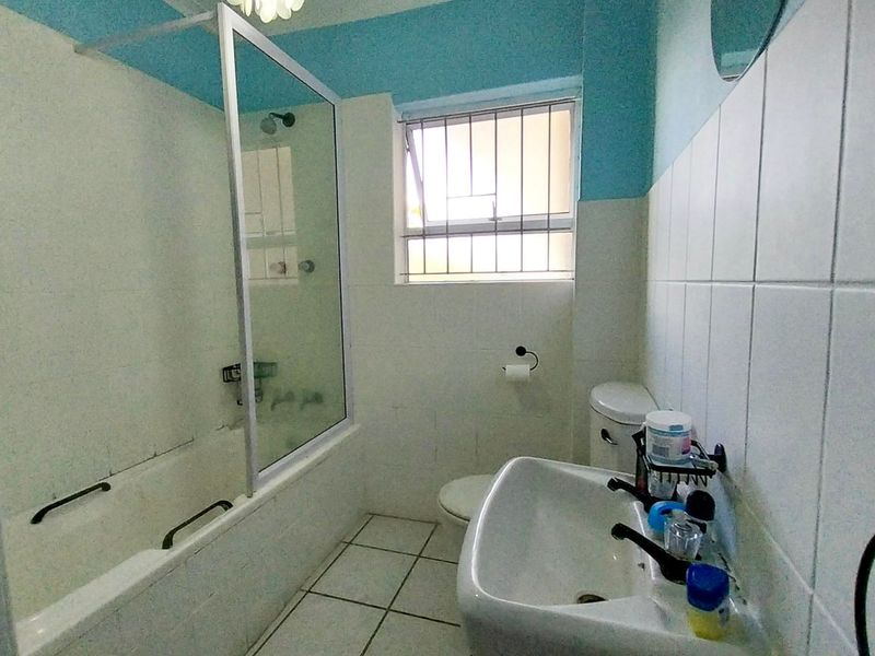 A functional bathroom featuring a bathtub with a glass screen, pedestal basin, and toilet, finished with tiled walls and flooring.
