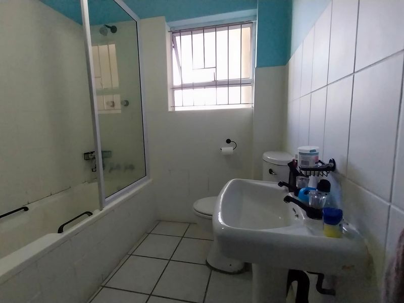 A functional bathroom featuring a pedestal basin, toilet, and a bathtub with a glass shower screen, finished with ceramic wall tiling.