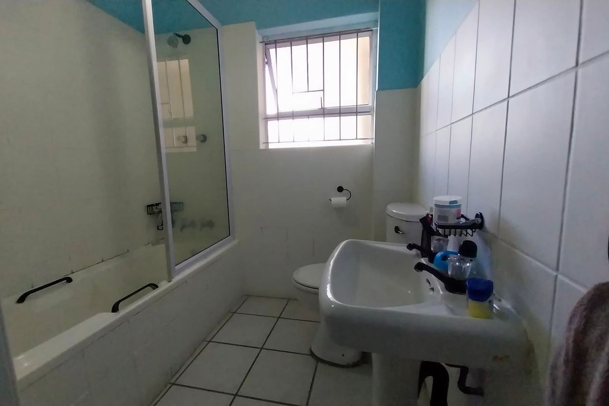 A functional bathroom featuring a pedestal basin, toilet, and a bathtub with a glass shower screen, finished with ceramic wall tiling.