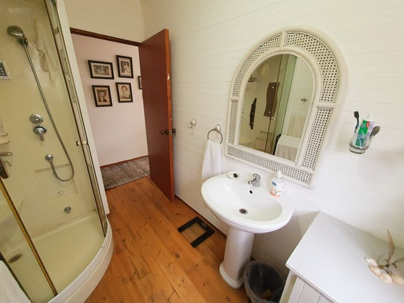 A functional bathroom featuring a pedestal sink, shower enclosure, and timber flooring with classic wall paneling details.