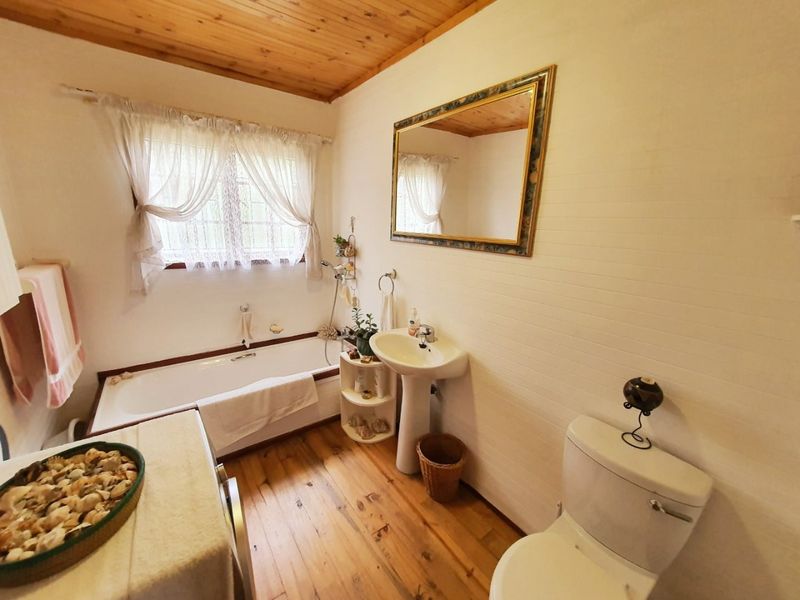 A bathroom featuring a bathtub, pedestal basin, and toilet, complemented by timber flooring and a natural wood ceiling finish.