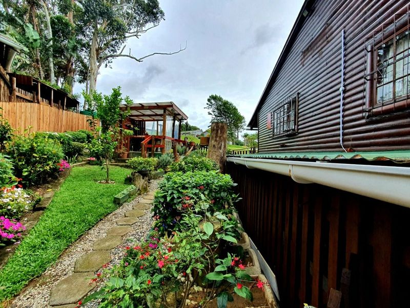 A well-maintained rear garden area featuring a stone pathway, lush landscaping, and a timber-clad exterior wall with security bars on the windows.