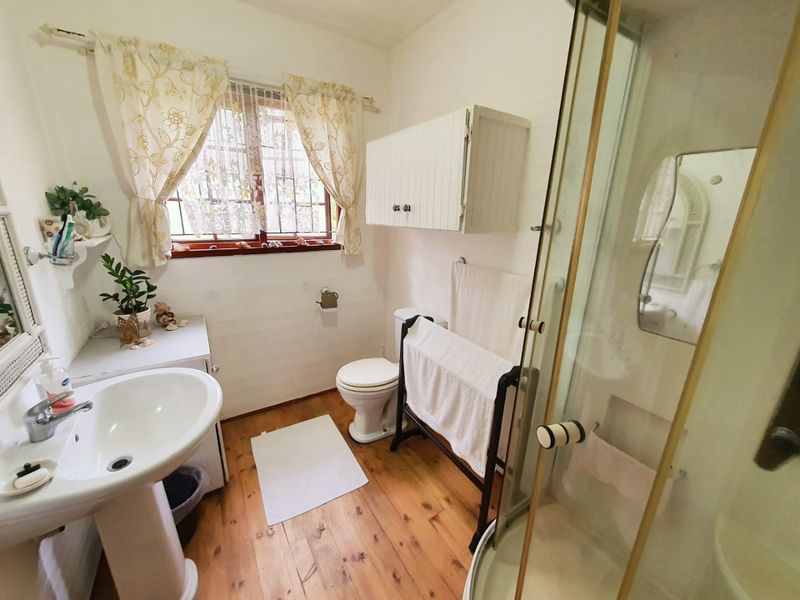 A functional bathroom featuring a pedestal basin, shower enclosure, toilet, and wall-mounted storage cabinet with timber flooring.