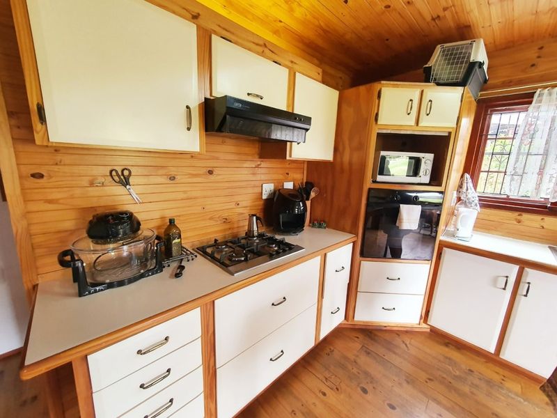 A rustic kitchen featuring timber wall cladding, cabinetry, and ceiling, equipped with a gas hob, extractor fan, and built-in oven.