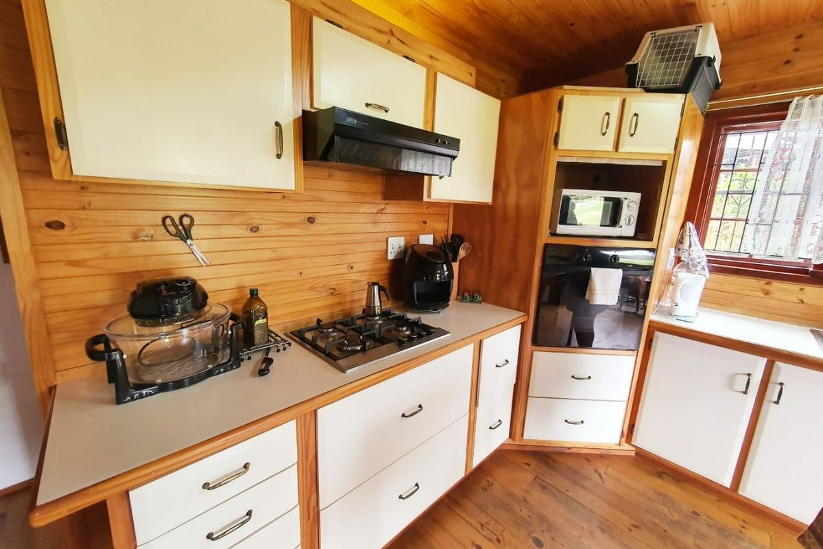 A rustic kitchen featuring timber wall cladding, cabinetry, and ceiling, equipped with a gas hob, extractor fan, and built-in oven.