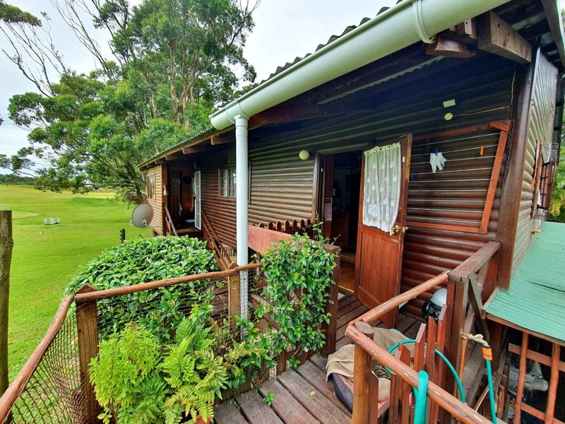 A rustic timber-clad exterior balcony featuring wooden decking and railings, overlooking a green landscape.
