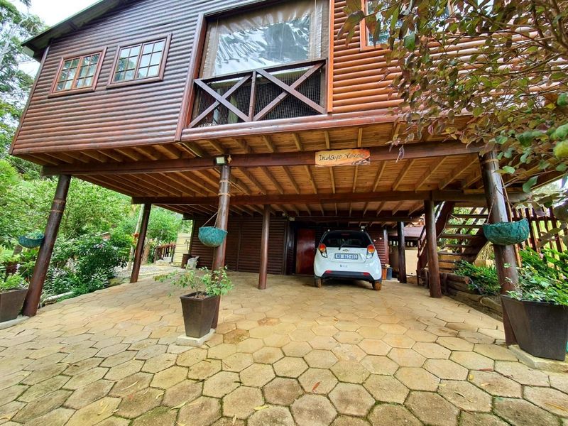 A stilted timber townhouse featuring a covered ground-level parking area with paved driveway and an elevated balcony above.