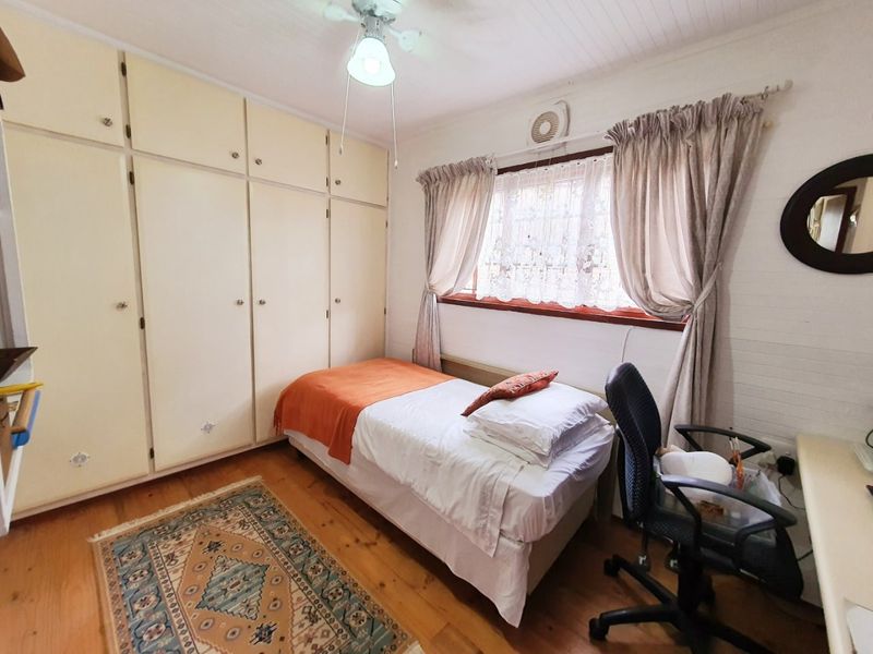 A functional bedroom featuring timber flooring, built-in cupboards, and a ceiling fan, offering a practical space with classic finishes.