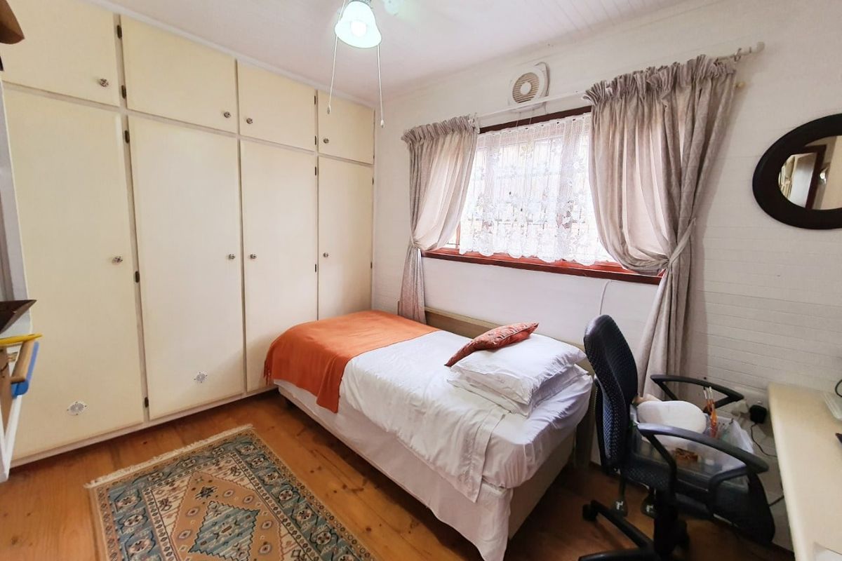 A functional bedroom featuring timber flooring, built-in cupboards, and a ceiling fan, offering a practical space with classic finishes.