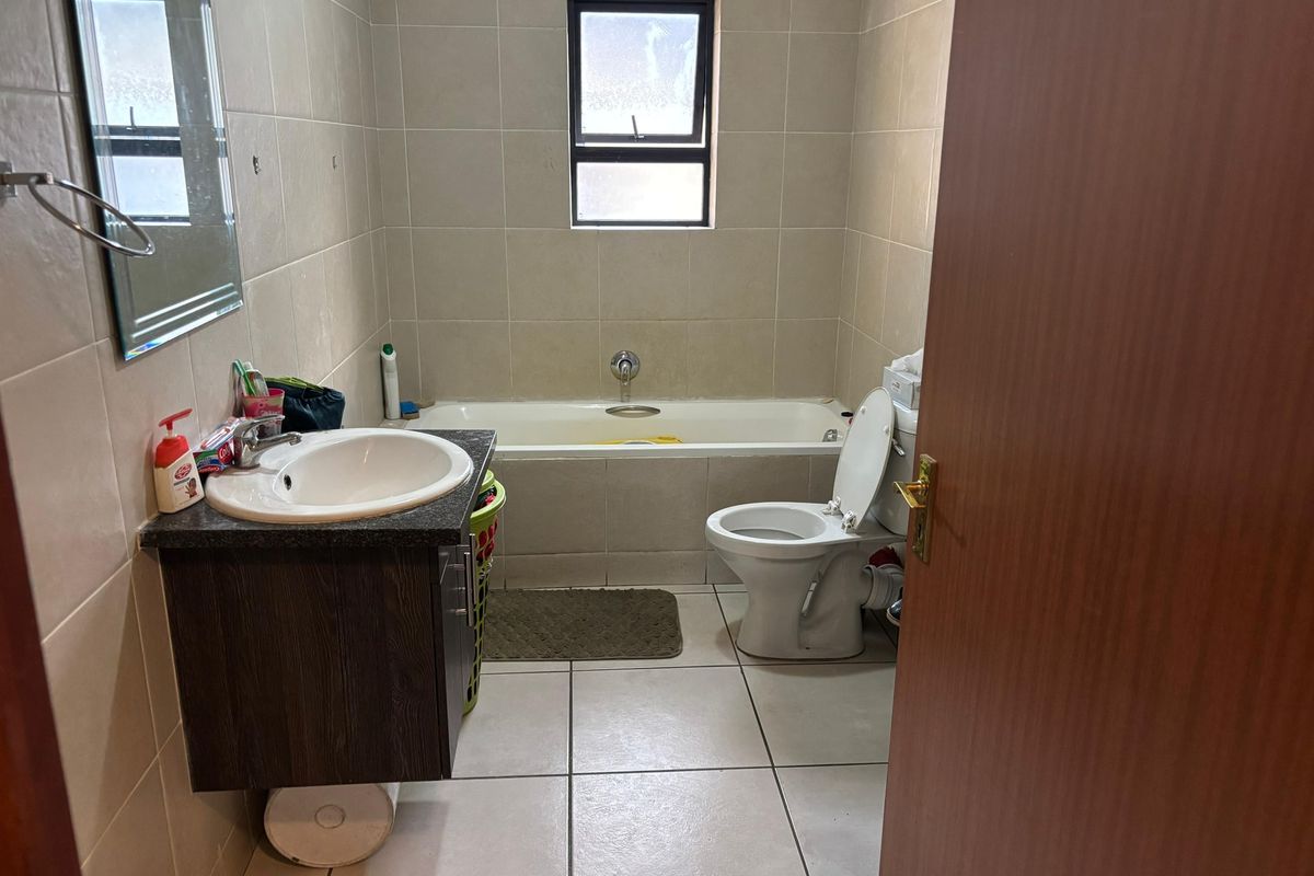 A functional bathroom featuring a built-in bathtub, a wall-mounted vanity with a basin, and tiled walls and flooring.