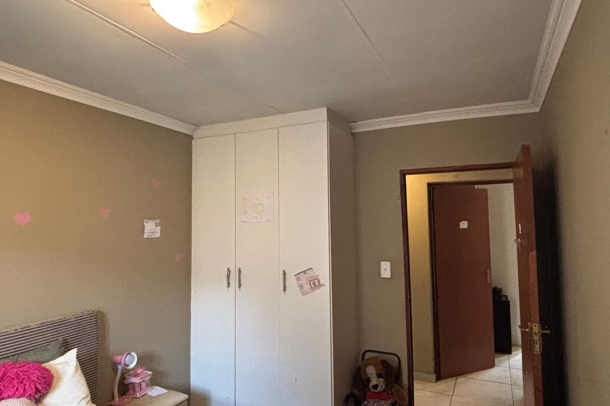 A bedroom featuring built-in white cabinetry, crown molding, and a ceiling light fixture, with an adjacent doorway leading to a tiled hallway.