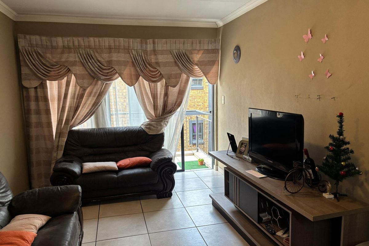A living room featuring tiled flooring, crown molding, and a sliding glass door providing access to a small balcony.