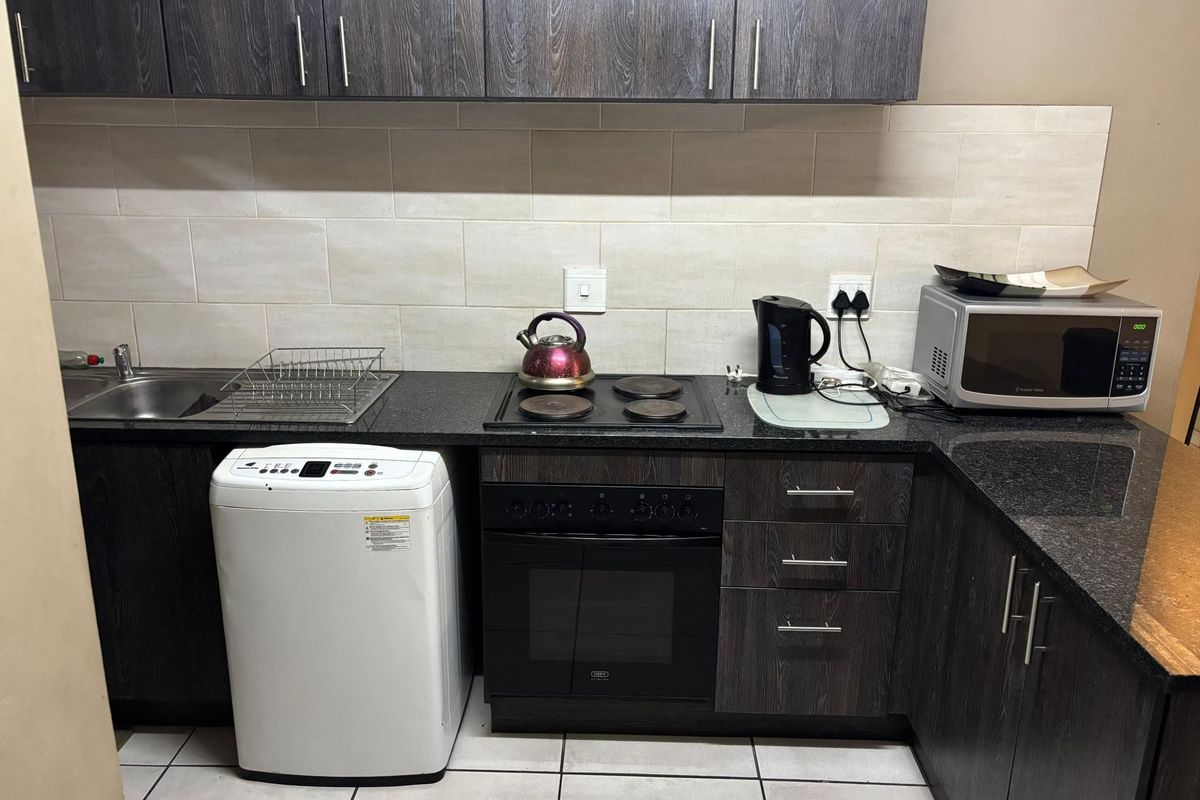 A functional kitchen featuring dark wood cabinetry, granite countertops, a built-in oven with hob, and a stainless steel sink with tiled splashback.