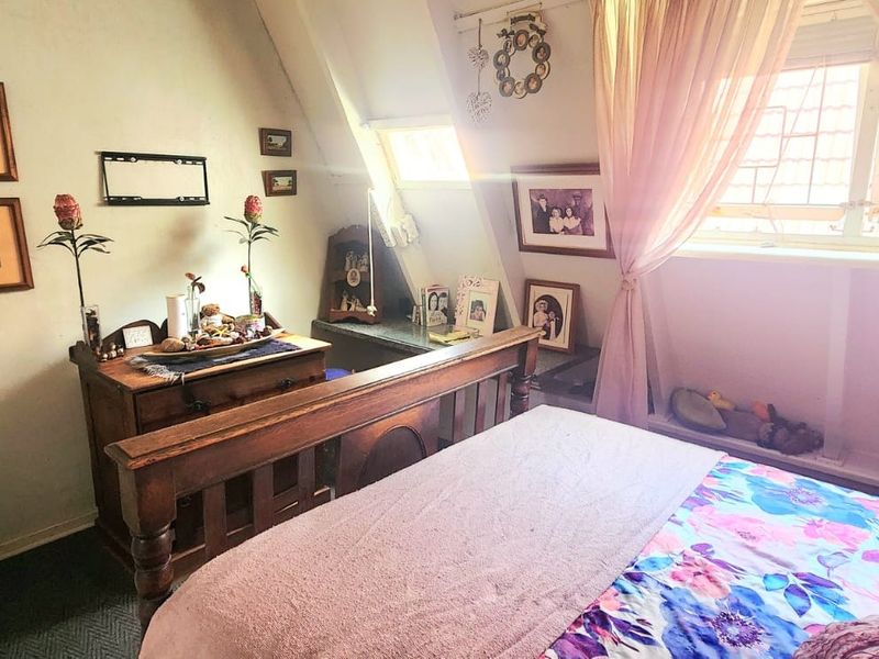 A cozy bedroom featuring a sloped ceiling and a leaded glass window, providing natural light and a unique architectural character.