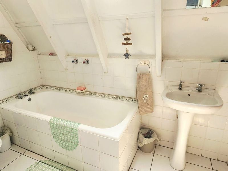 A compact bathroom featuring a bathtub, pedestal basin, and toilet, finished with white wall and floor tiles under exposed rafters.