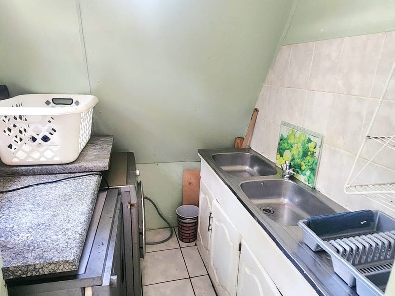 A compact laundry area featuring a double stainless steel sink, laminate countertops, built-in cabinetry, and tiled splashbacks.