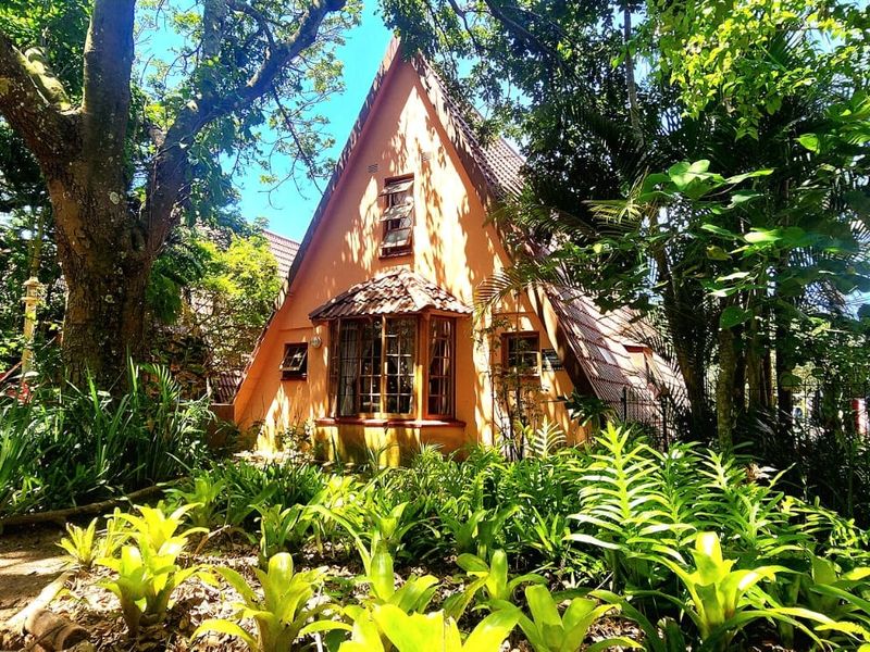 A charming A-frame townhouse exterior featuring a prominent bay window, set within a lush, mature garden environment.
