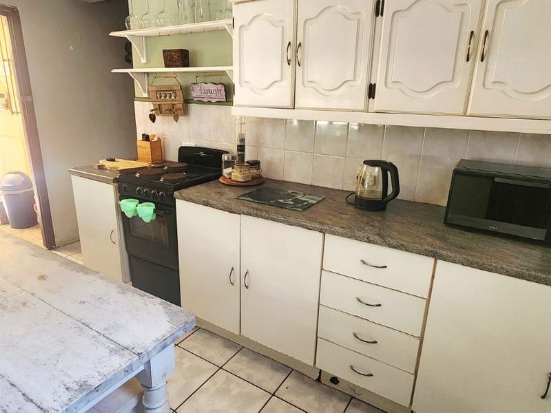 A functional kitchen featuring white cabinetry, laminate countertops, tiled backsplash, and ceramic flooring, with direct access to an outdoor patio area.