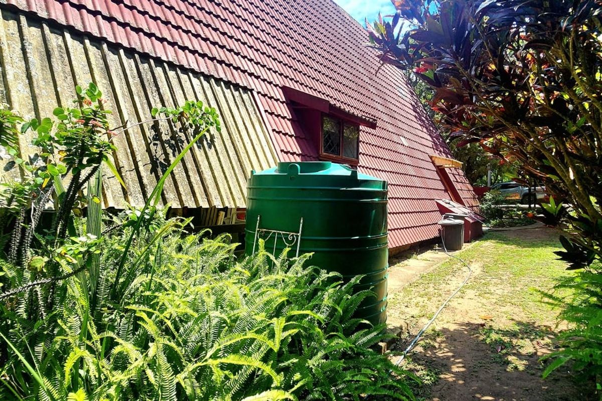 Rear exterior view of the townhouse featuring a pitched roof design, a large water storage tank, and established garden landscaping.