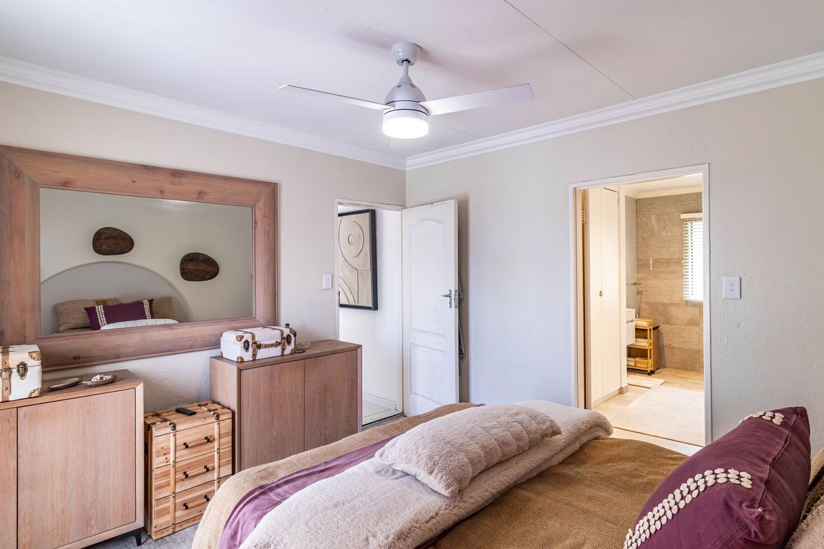 A well-maintained bedroom featuring a ceiling fan, coved cornicing, and direct access to an en-suite bathroom.