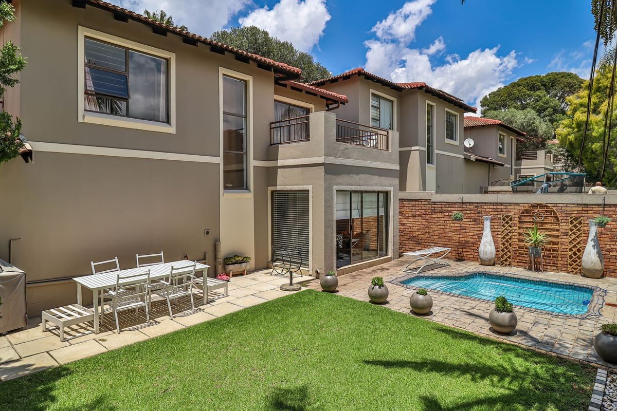 Rear exterior view of the townhouse featuring a private swimming pool, paved patio area, manicured lawn, and a balcony overlooking the garden.