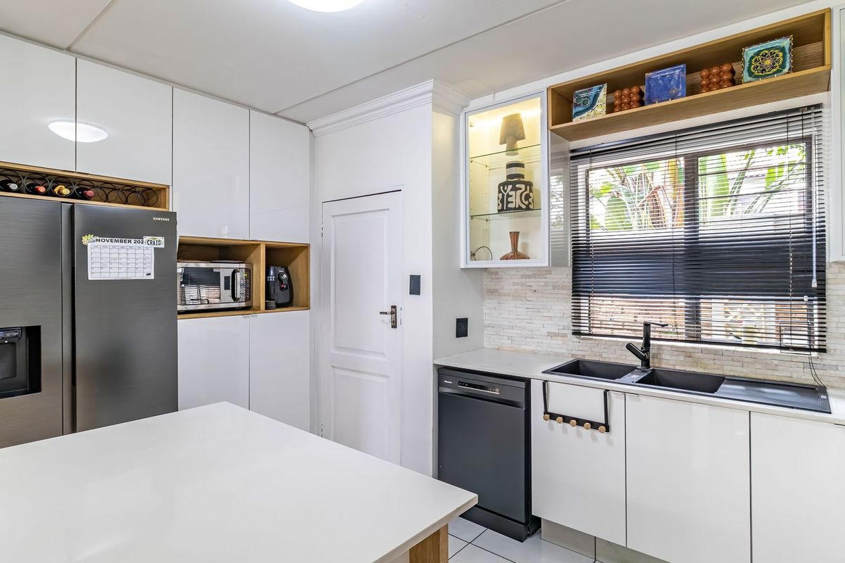 Modern kitchen featuring white gloss cabinetry, stone countertops, a double basin sink, integrated dishwasher, and built-in microwave with stylish glass display shelving.