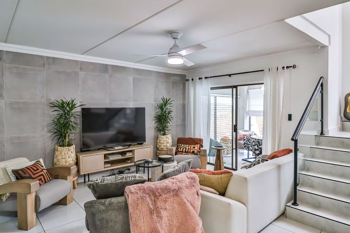 Modern living room featuring large format wall tiles, a ceiling fan, and a staircase with a contemporary glass balustrade leading to the upper level.