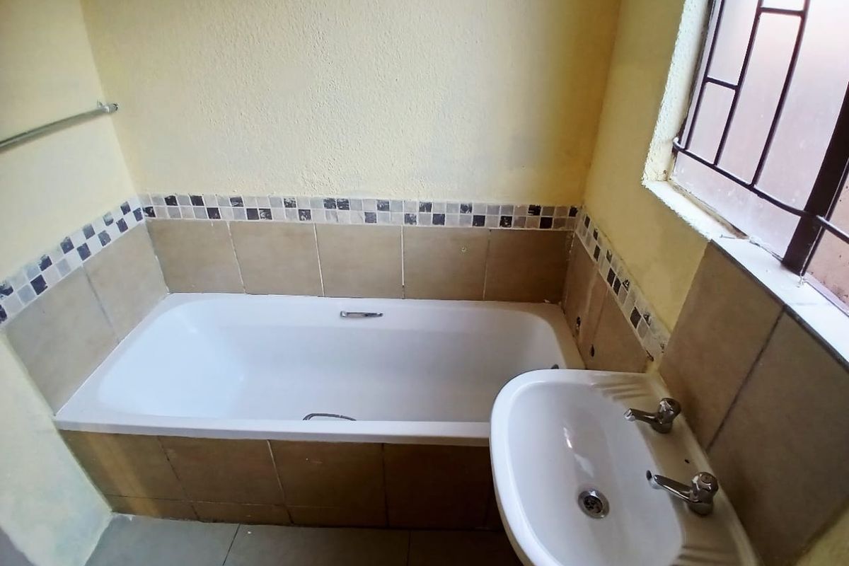 A dated bathroom featuring a built-in bathtub with tiled surround and a pedestal washbasin, requiring cosmetic updates to modernize the space.