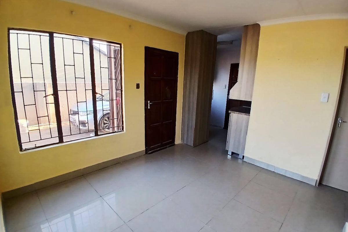 An empty living area featuring tiled flooring, security bars on the windows, and built-in cabinetry, offering a blank canvas for interior design.