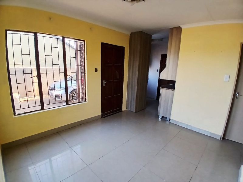 An empty living area featuring tiled flooring, security bars on the windows, and built-in cabinetry, offering a blank canvas for interior design.