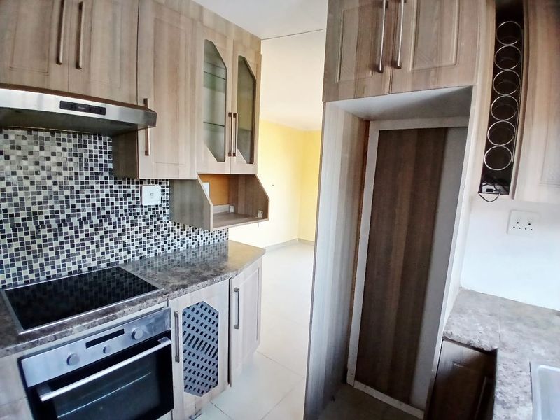 A functional kitchen featuring wood-look cabinetry, mosaic tile backsplash, built-in oven and hob, and dedicated space for a refrigerator.