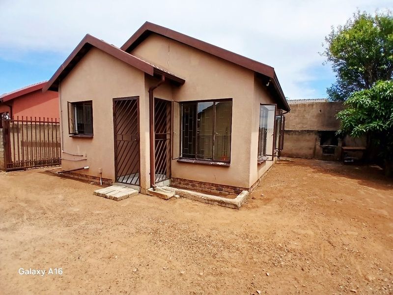 Rear view of a detached house featuring a brick exterior, security gates, and a built-in outdoor braai area set within an unlandscaped yard.