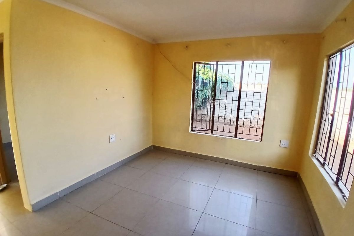 An empty bedroom featuring tiled flooring and windows fitted with security bars, requiring minor cosmetic updates and wall repairs.