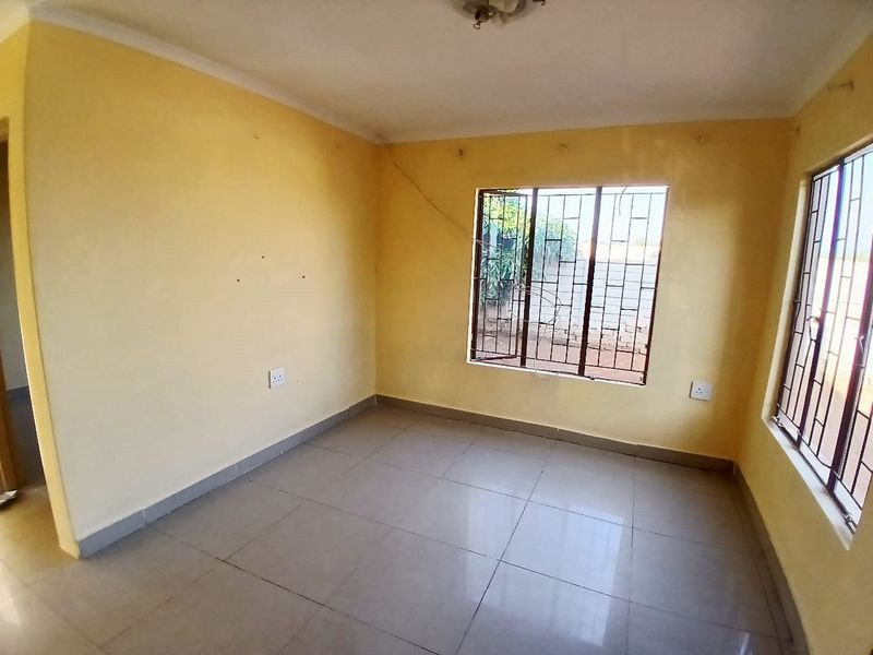 An empty bedroom featuring tiled flooring and windows fitted with security bars, requiring minor cosmetic updates and wall repairs.