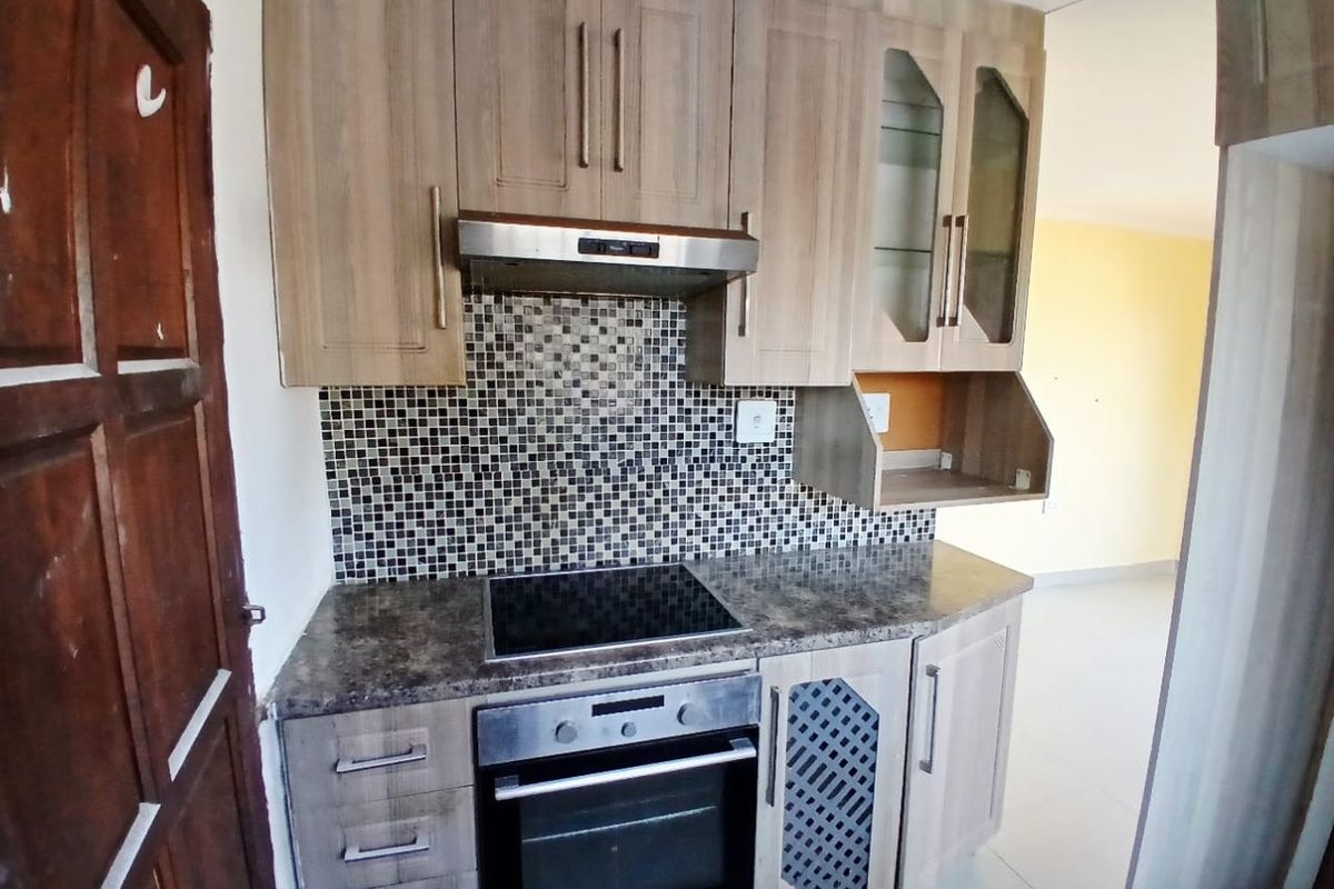 A compact kitchen featuring wood-look laminate cabinetry, a mosaic tile backsplash, built-in oven, electric hob, and an integrated extractor fan.