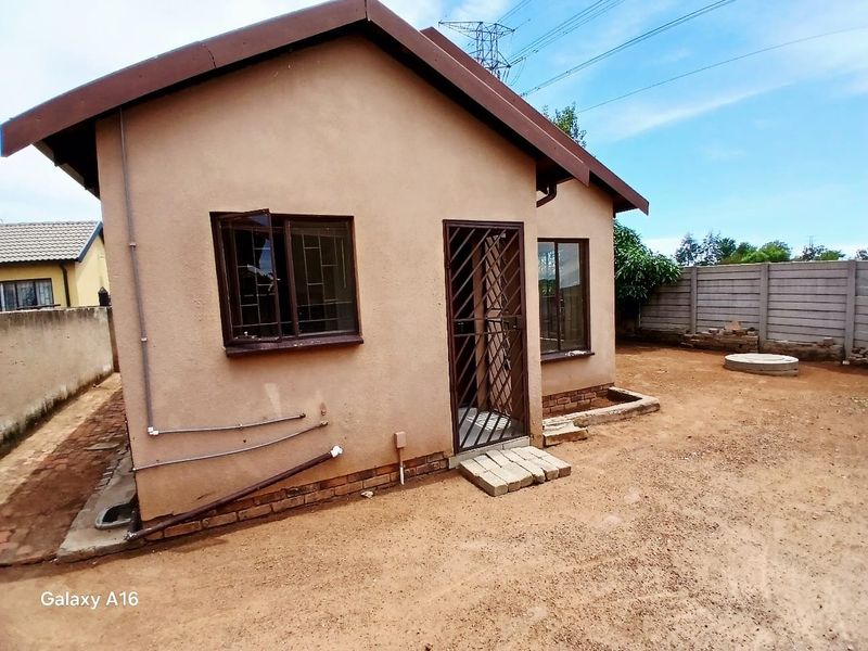 Rear view of the property featuring a simple facade, security gate, and precast concrete boundary wall with an unfinished dirt yard.