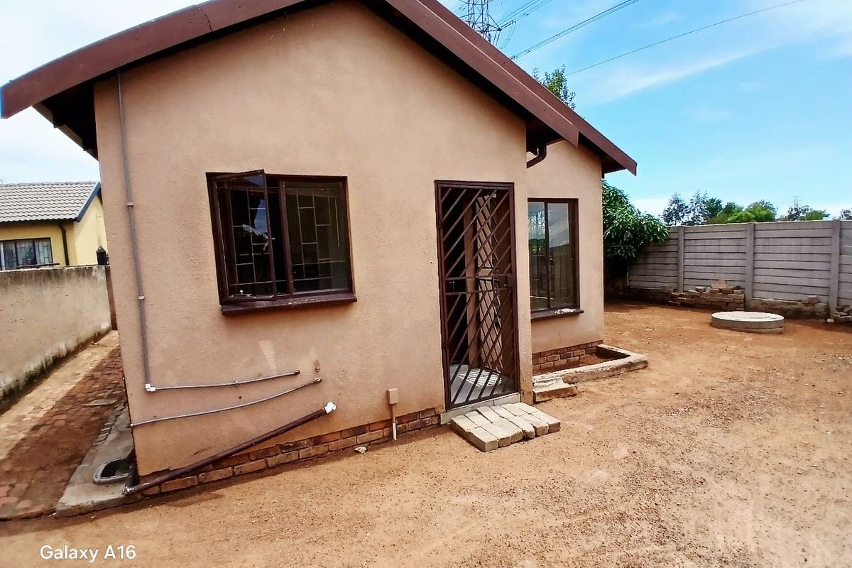 Rear view of the property featuring a simple facade, security gate, and precast concrete boundary wall with an unfinished dirt yard.