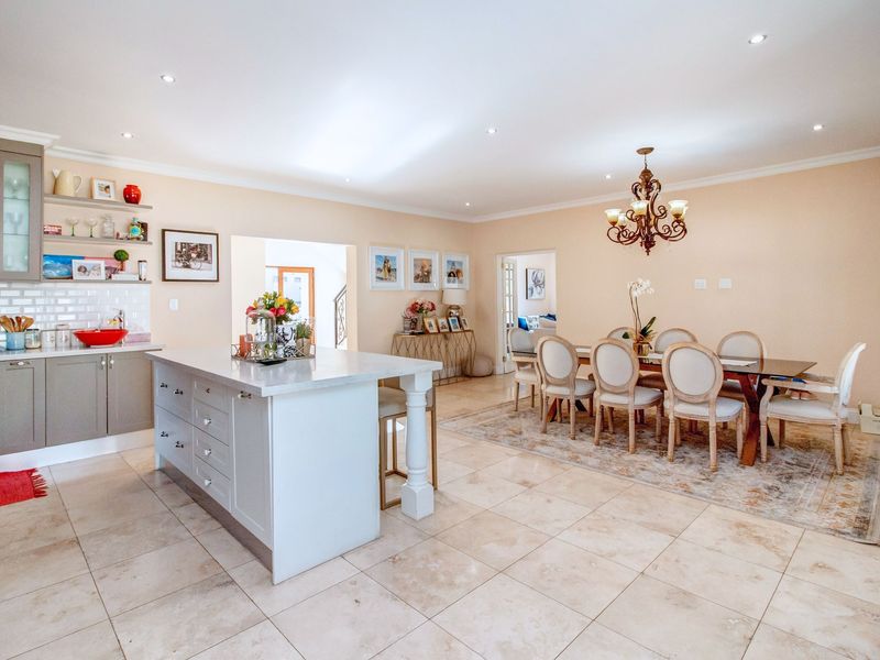 Spacious open-plan kitchen and dining area featuring a central island, stone countertops, subway tile backsplash, and neutral tiled flooring throughout.
