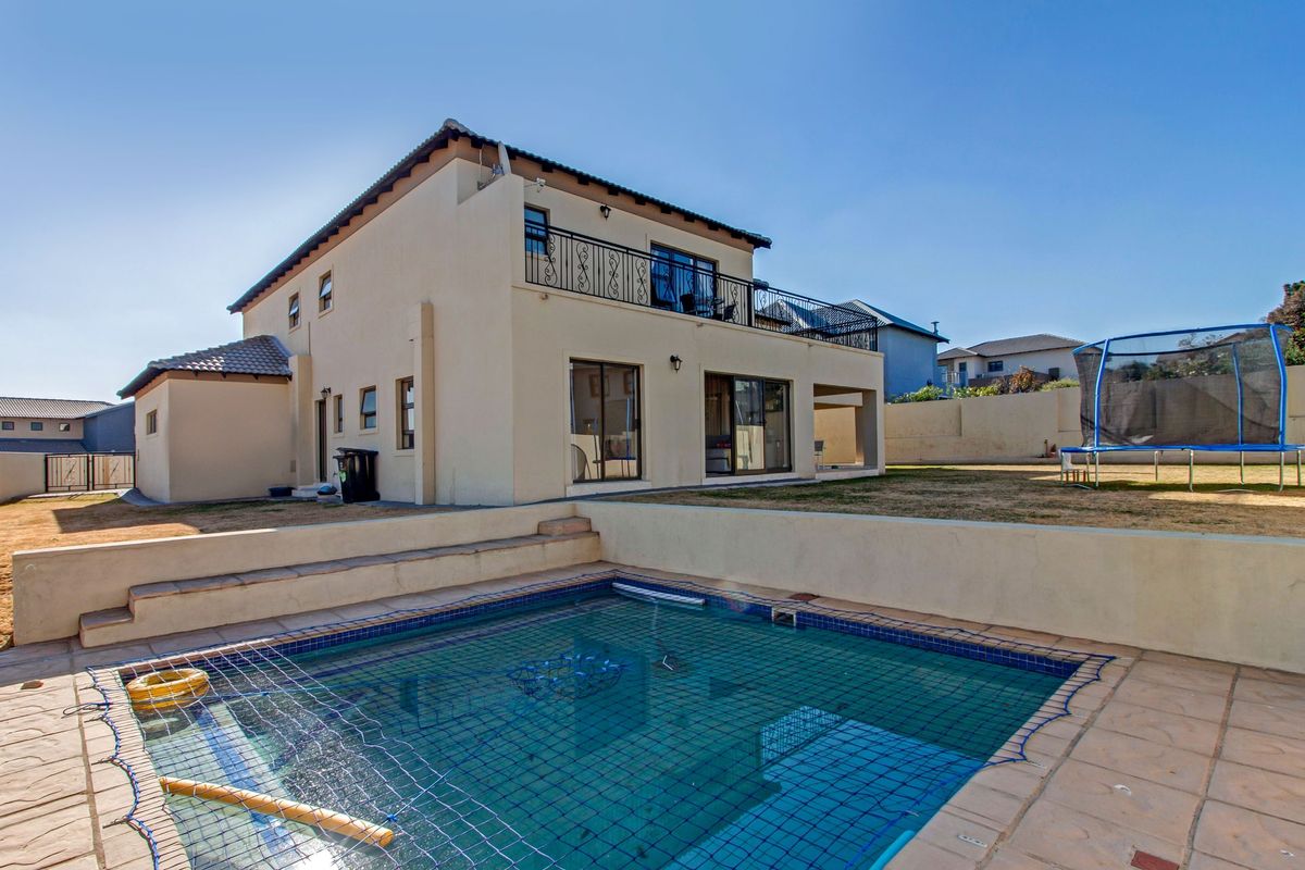 Rear view of a two-story house featuring a swimming pool with safety net, a tiled patio area, and an upper-level balcony with wrought iron railings.
