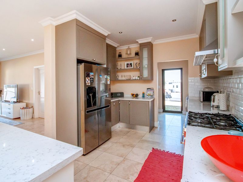 Modern kitchen featuring stone countertops, built-in cabinetry, gas hob with extractor fan, and tiled flooring, leading to an adjacent living area.