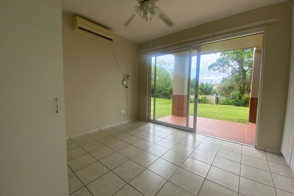 Empty living room featuring tiled floors, a ceiling fan, wall-mounted air conditioning, and sliding glass doors opening onto a patio and garden.