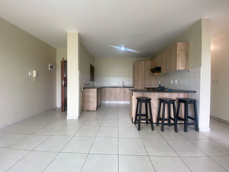 Open-plan kitchen and living area featuring light wood-finish cabinetry, laminate countertops, an extractor fan, and neutral tiled flooring throughout.