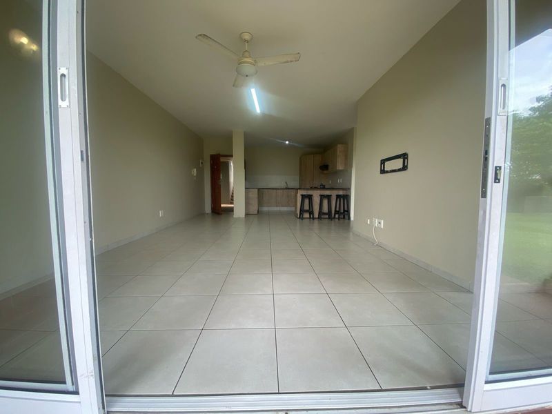 Spacious open-plan living and kitchen area featuring neutral tiled flooring, a ceiling fan, and modern built-in cabinetry, accessible via sliding glass doors.