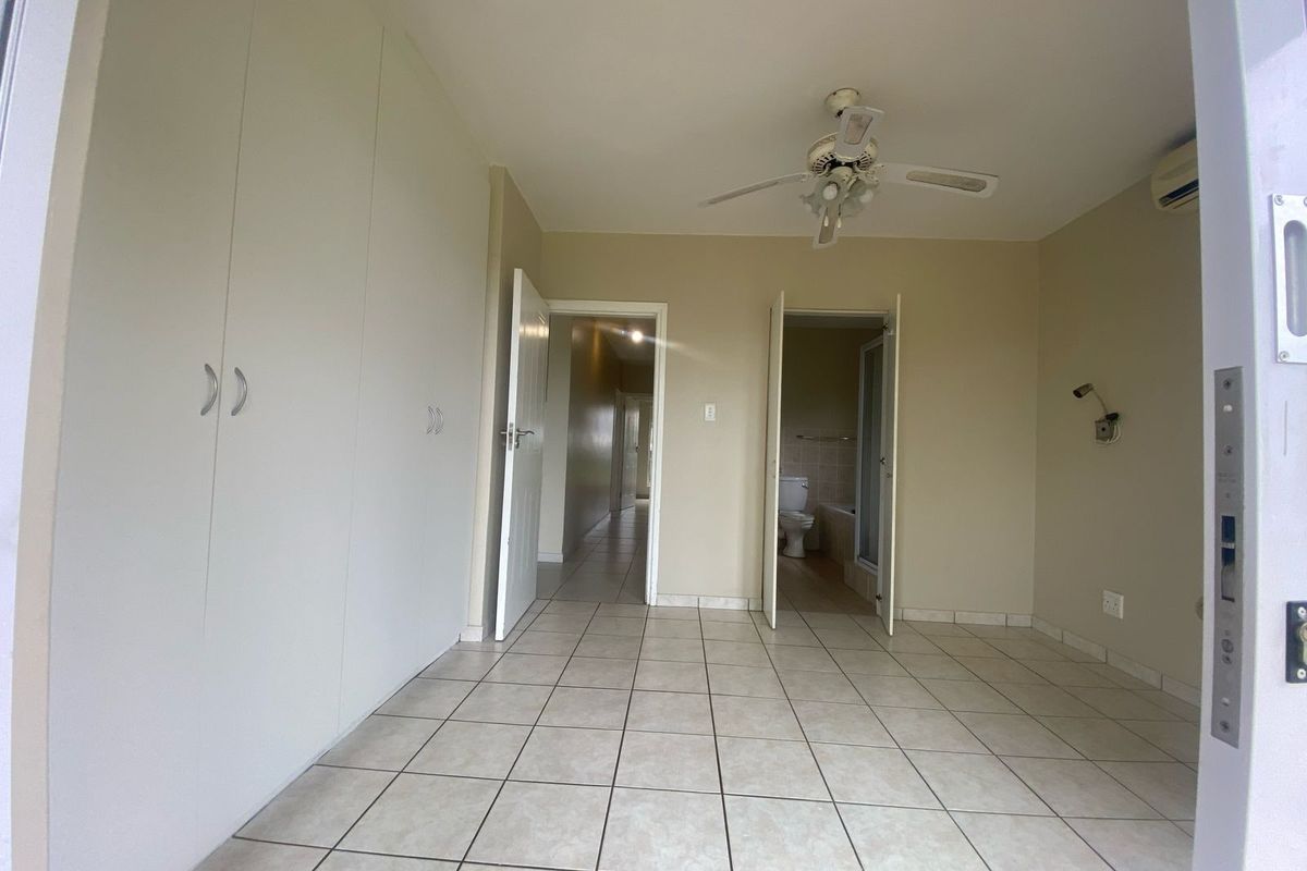 An empty bedroom featuring tiled flooring, built-in cupboards, a ceiling fan, and an air conditioning unit, with direct access to an en-suite bathroom.
