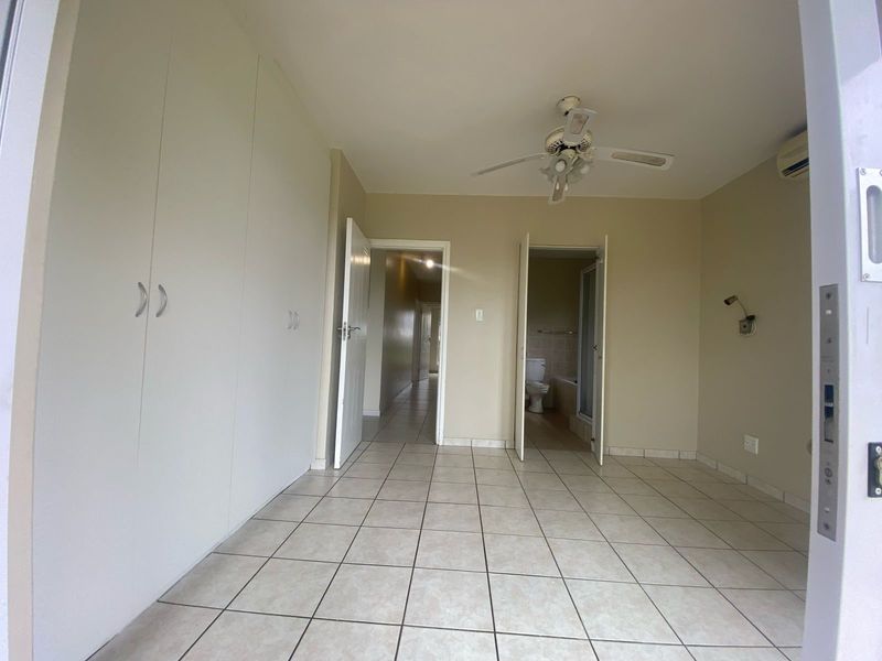 An empty bedroom featuring tiled flooring, built-in cupboards, a ceiling fan, and an air conditioning unit, with direct access to an en-suite bathroom.