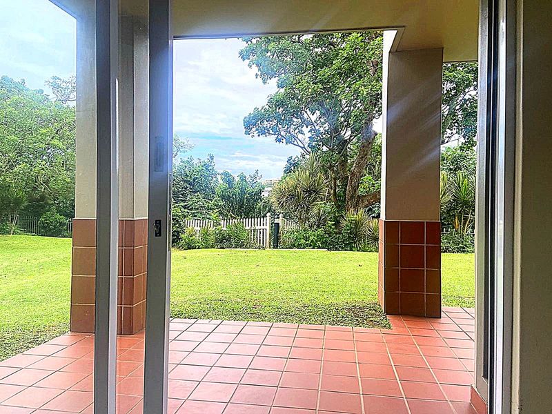 A covered patio area featuring tiled flooring and support columns, providing direct access to a private garden space through sliding glass doors.