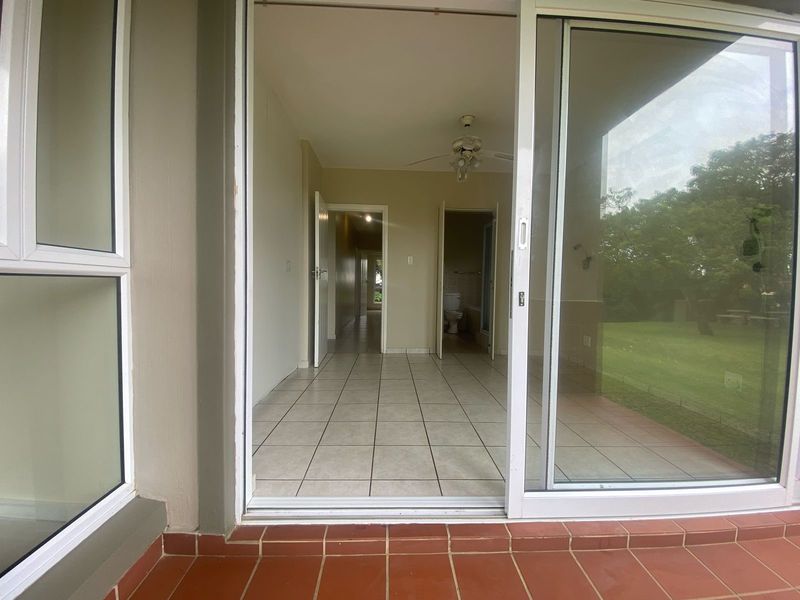 View from a tiled patio through a sliding glass door into an empty interior hallway and bathroom area.