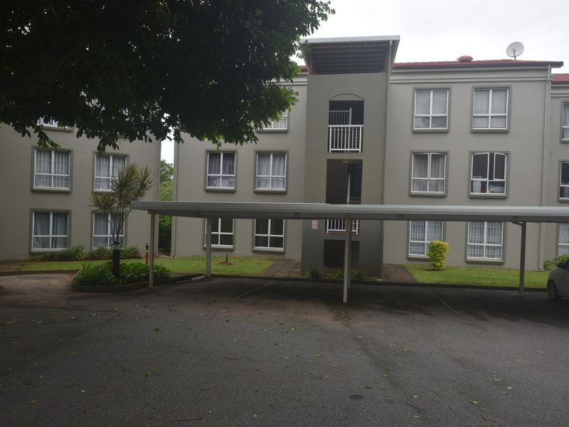 Exterior view of a multi-story apartment complex featuring a covered carport area and paved driveway access.